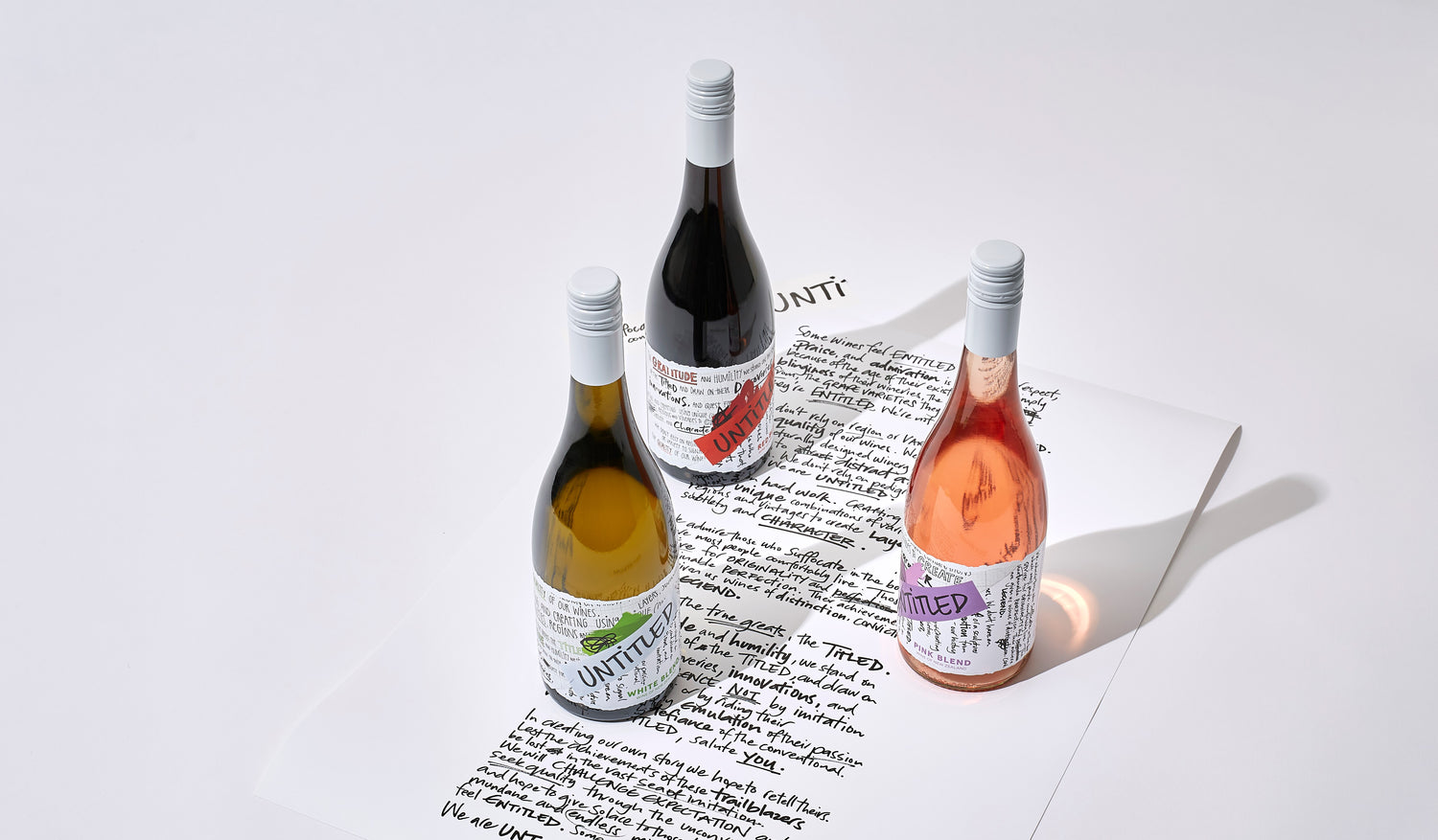 Untitled Wines hand written manifesto on paper with three bottles on Untitled Wines wine on top of it - the red blend, pink blend and white blend. Wines of New Zealand. Best wine online